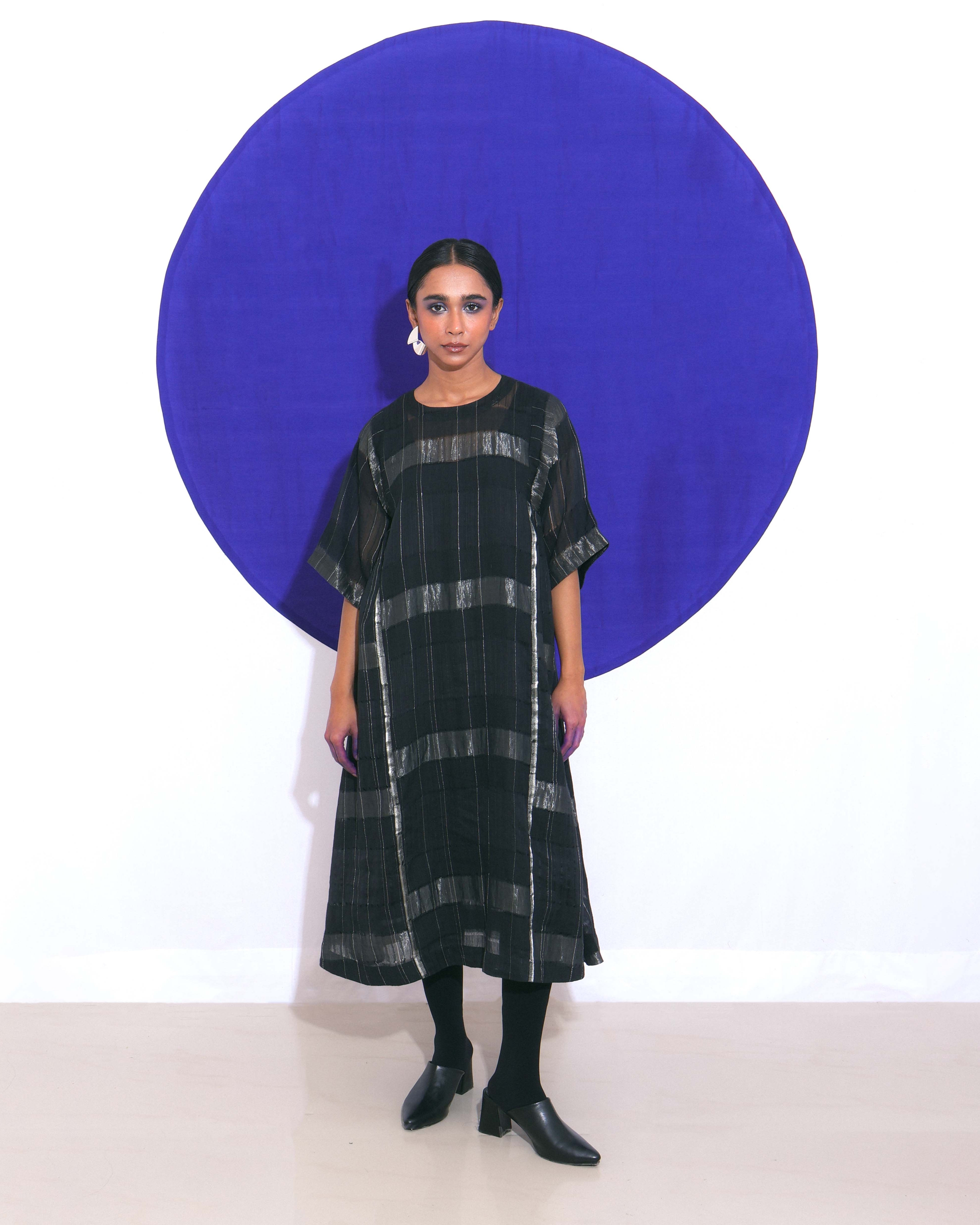 The "Shoonyata Blockstripe Panelled Dress" is an elegant dress made from handwoven silk. It features a round neckline with notched detailing, and wide, three-quarter-length sleeves for a relaxed fit.