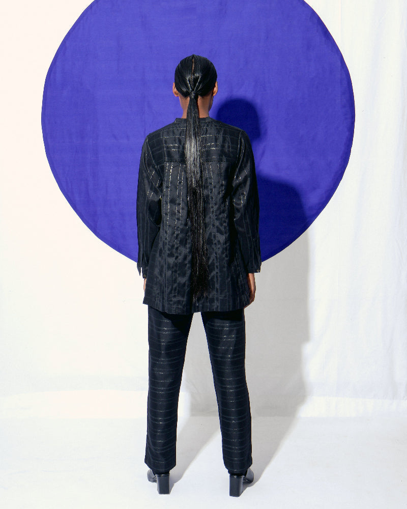 The Shoonyata Burnished Stripe Straight Pants is crafted from silk fabric. The straight-cut pants feature a relaxed silhouette, merging comfort with a refined style. The rich black shade, combined with the burnished sheen of the zari stripes.
