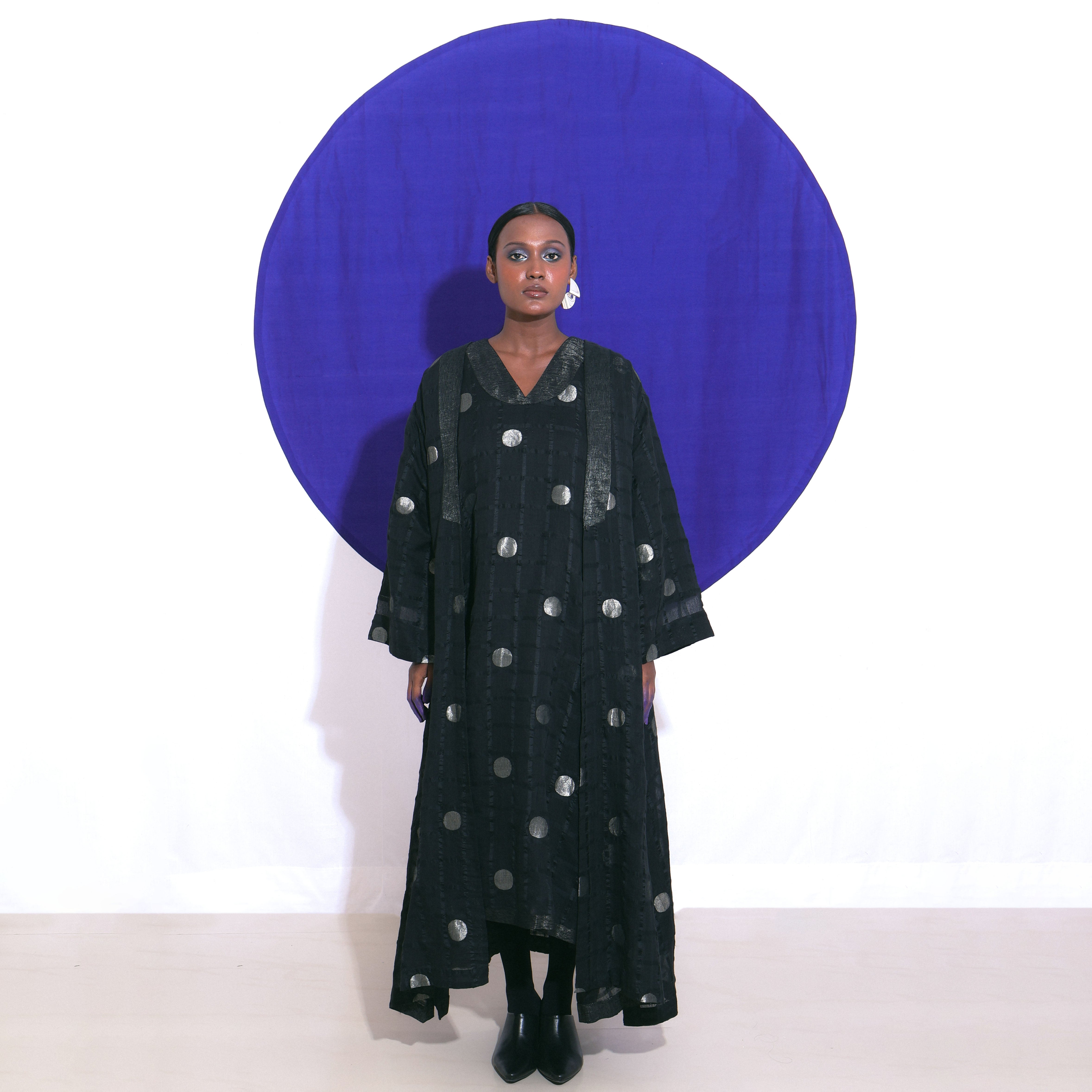 The Shoonyata Polka Dots Sheer Choga Overlay features an oversized, flowing silhouette made from handwoven silk. Crafted using intricate Jacquard Jamdani weaving techniques