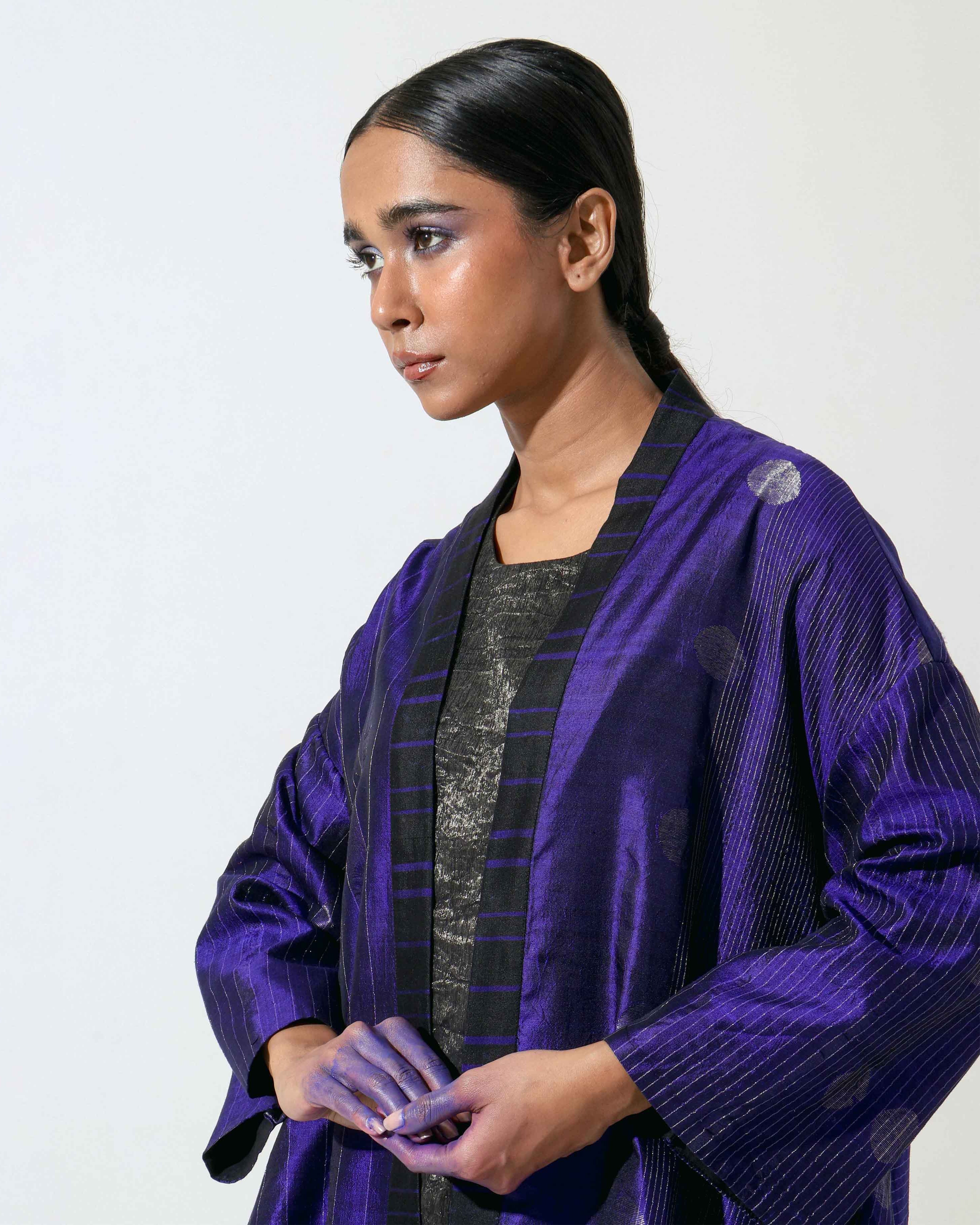 The Shoonyata Flared Kimono Jacket is a luxurious piece made from handwoven silk using the Jacquard Jamdani technique. It features intricate silver zari work and a rich royal Blue hue, enhancing its elegant appearance.