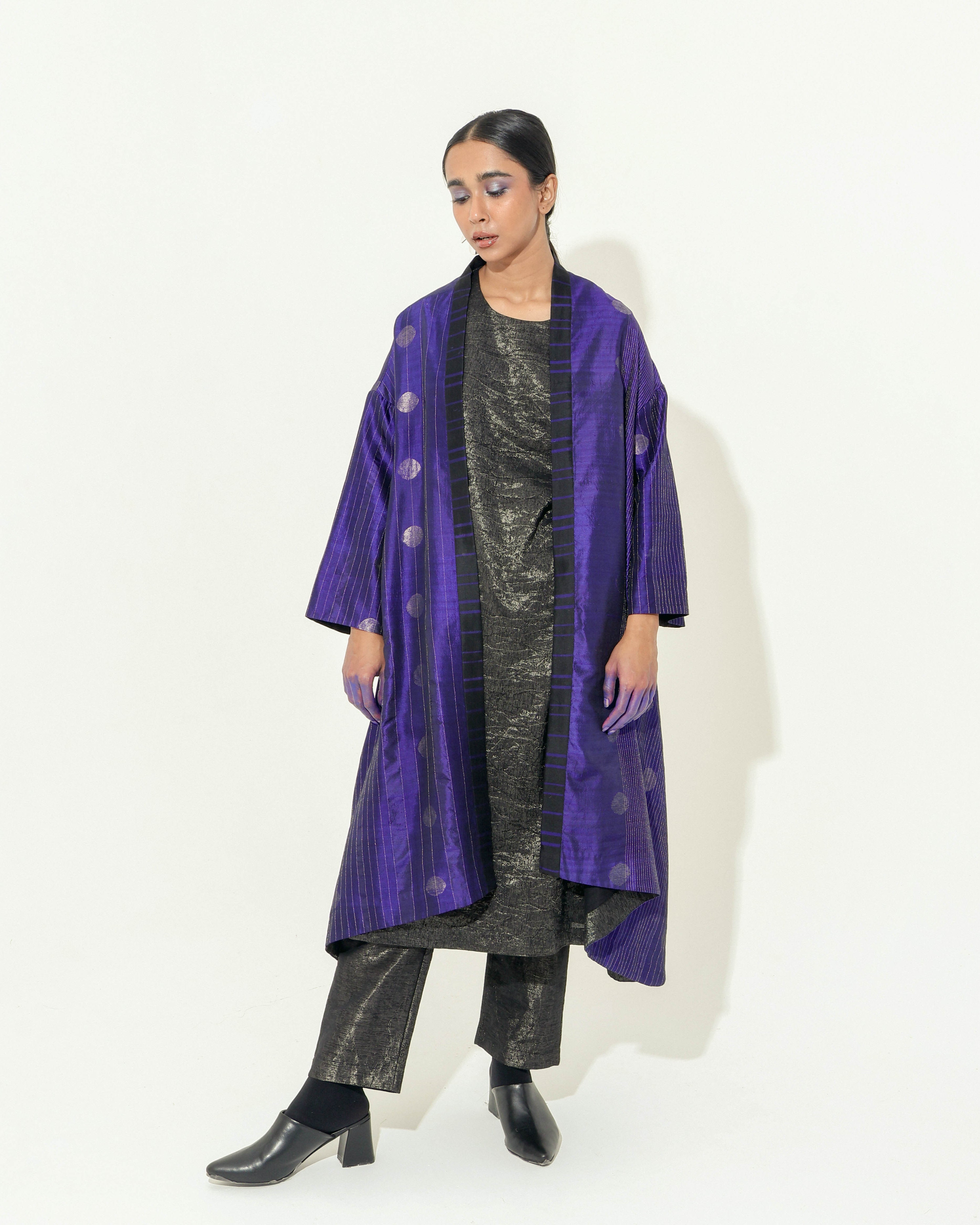 The Shoonyata Flared Kimono Jacket is a luxurious piece made from handwoven silk using the Jacquard Jamdani technique. It features intricate silver zari work and a rich royal Blue hue, enhancing its elegant appearance.