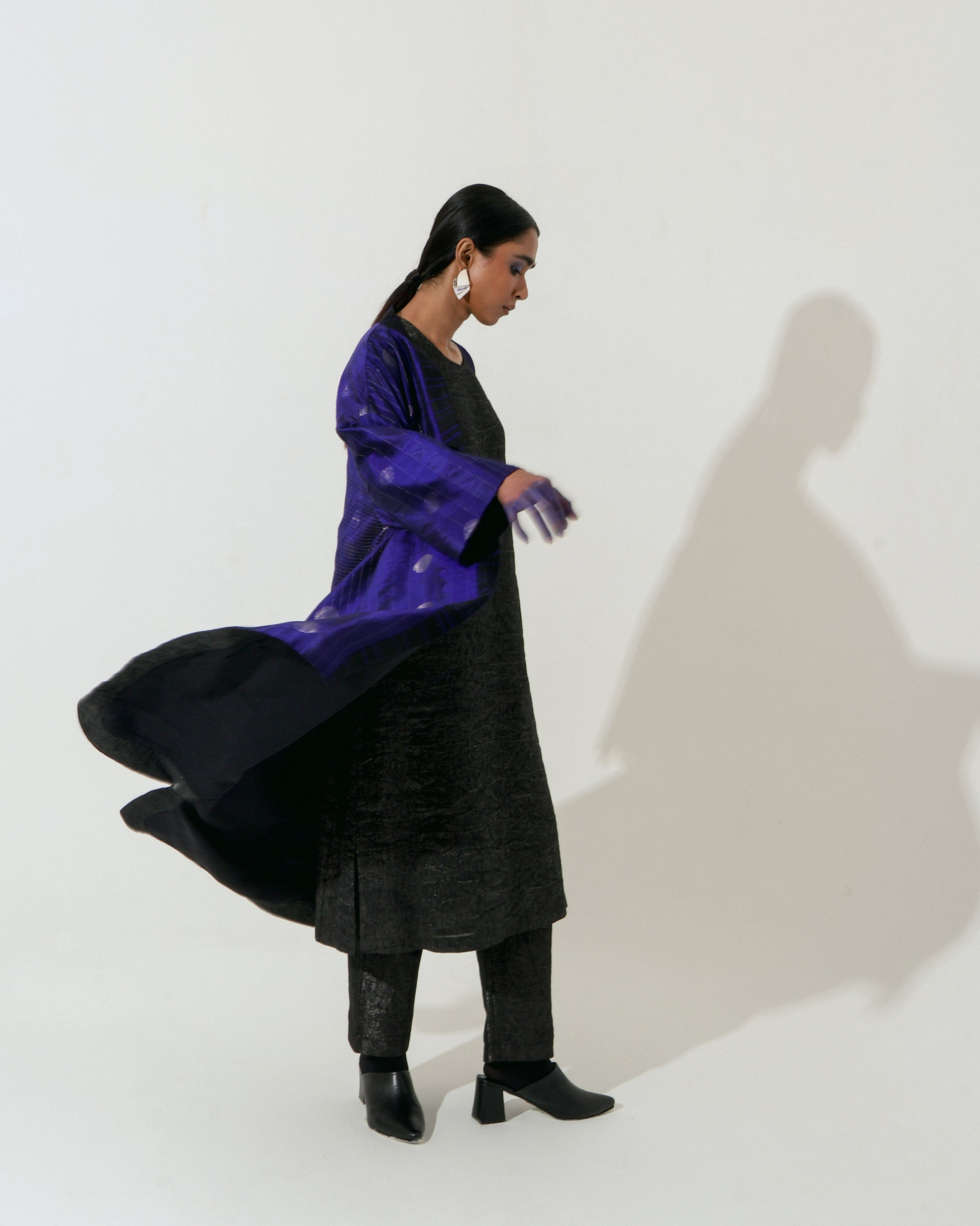 The Shoonyata Flared Kimono Jacket is a luxurious piece made from handwoven silk using the Jacquard Jamdani technique. It features intricate silver zari work and a rich royal Blue hue, enhancing its elegant appearance.
