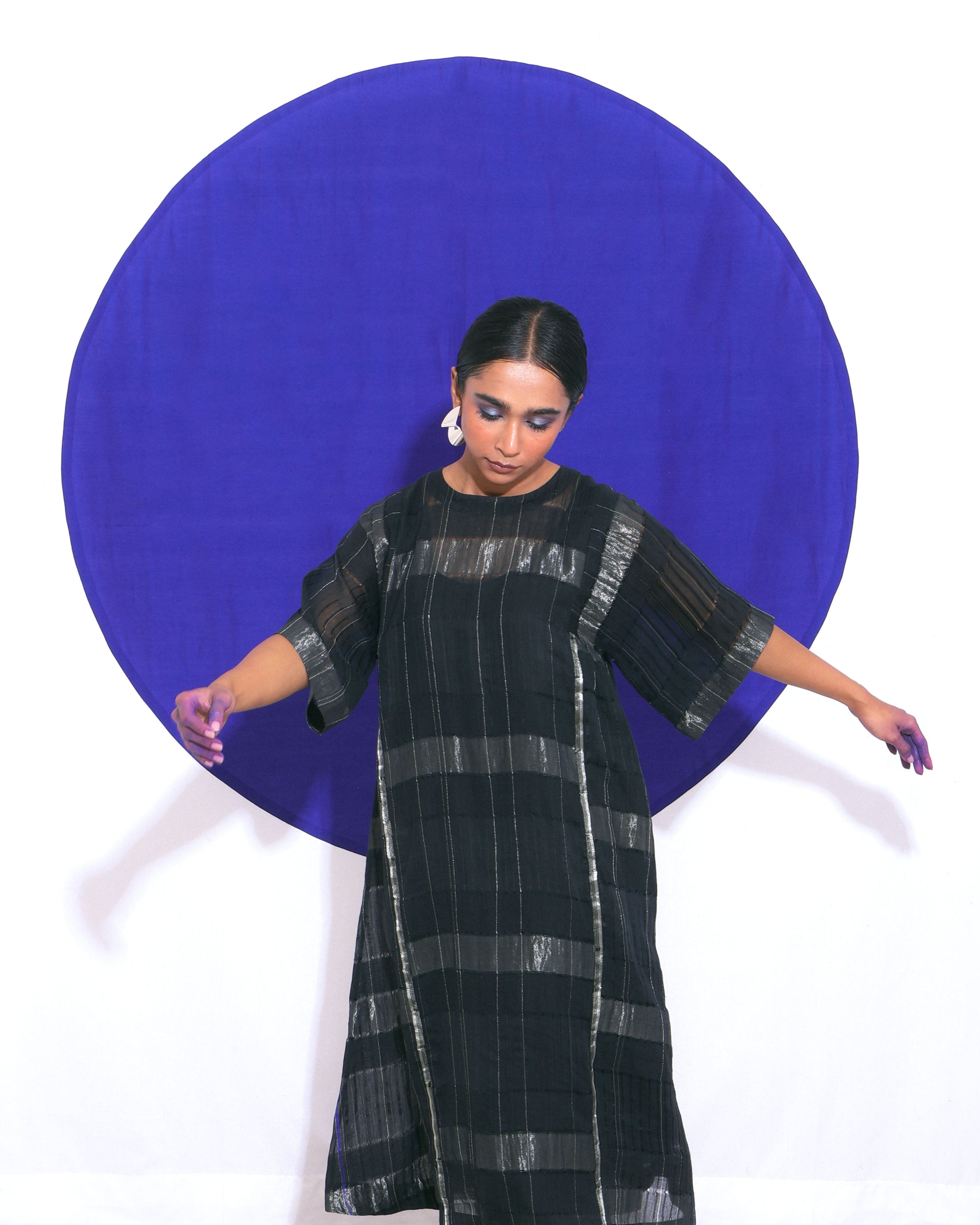 The "Shoonyata Blockstripe Panelled Dress" is an elegant dress made from handwoven silk. It features a round neckline with notched detailing, and wide, three-quarter-length sleeves for a relaxed fit.