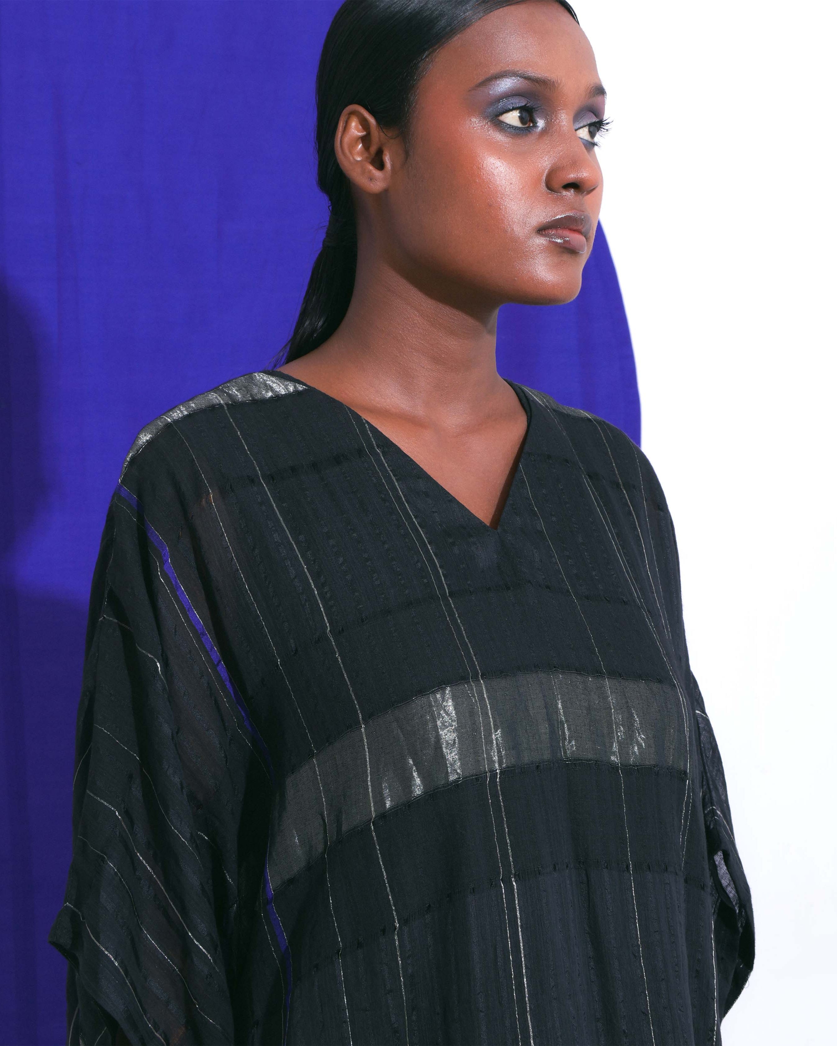 The Shoonyata Block Stripe Sheer Kaftan is a stylish, free-flowing garment made from handwoven silk. It features a relaxed, oversized silhouette, modest V-neckline, and wide elbow-length sleeves.