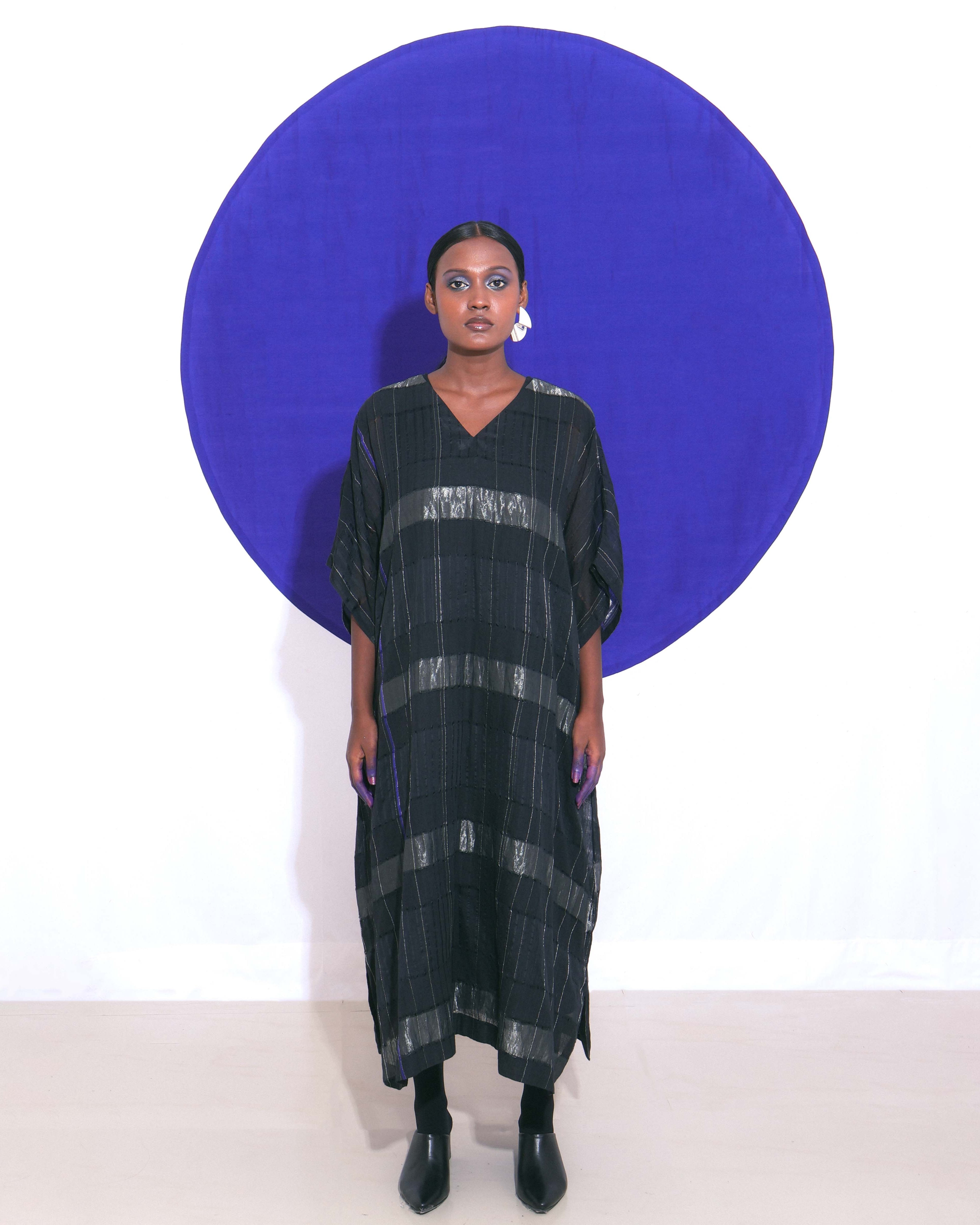 The Shoonyata Block Stripe Sheer Kaftan is a stylish, free-flowing garment made from handwoven silk. It features a relaxed, oversized silhouette, modest V-neckline, and wide elbow-length sleeves.