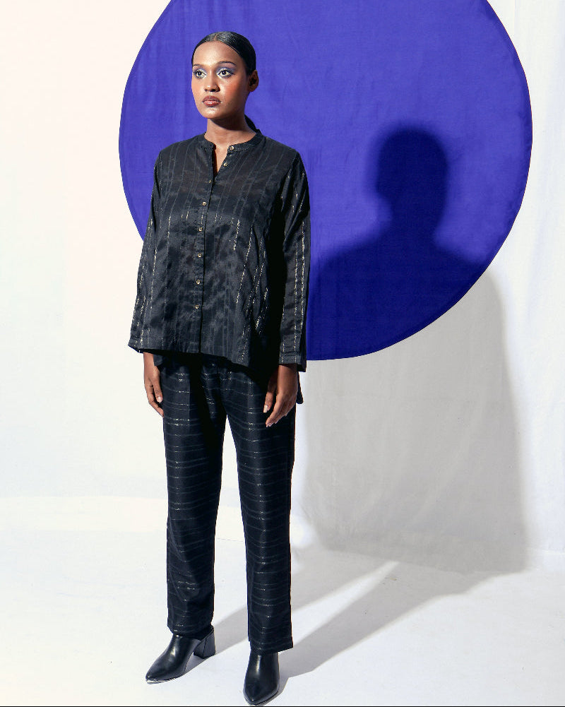 The Shoonyata Burnished Stripe Straight Pants is crafted from silk fabric. The straight-cut pants feature a relaxed silhouette, merging comfort with a refined style. The rich black shade, combined with the burnished sheen of the zari stripes. 