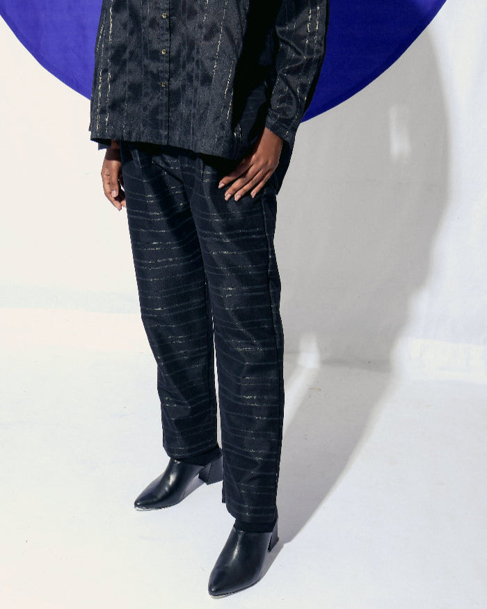 The Shoonyata Burnished Stripe Straight Pants is crafted from silk fabric. The straight-cut pants feature a relaxed silhouette, merging comfort with a refined style. The rich black shade, combined with the burnished sheen of the zari stripes. 