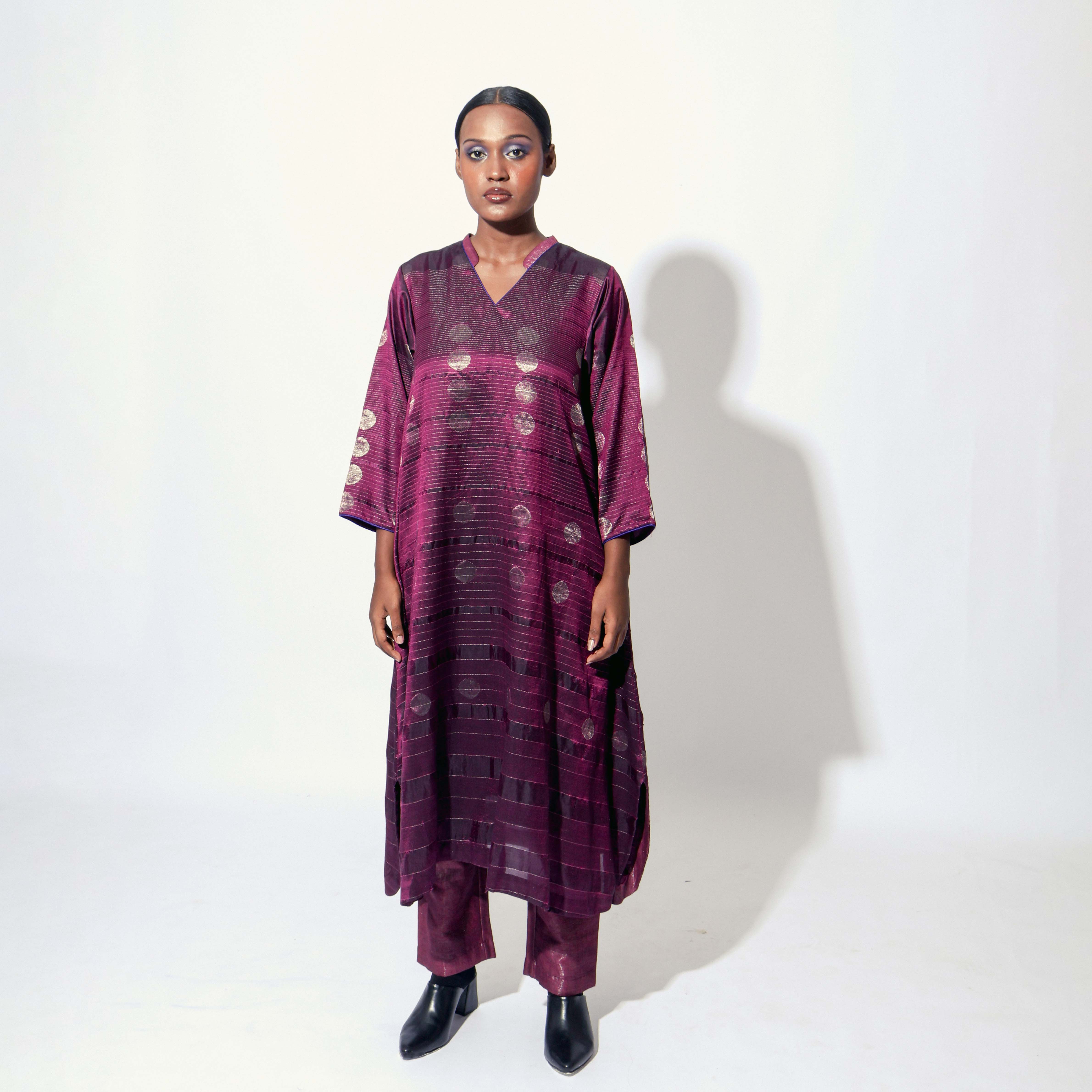 The Shoonyata Gradient Circle Flared Dress is an elegant handwoven silk piece utilizing the Jacquard Jamdani technique. It features a flattering A-line silhouette that extends to a midi length, complemented by a modest V-neckline and wide, three-quarter-length sleeves.