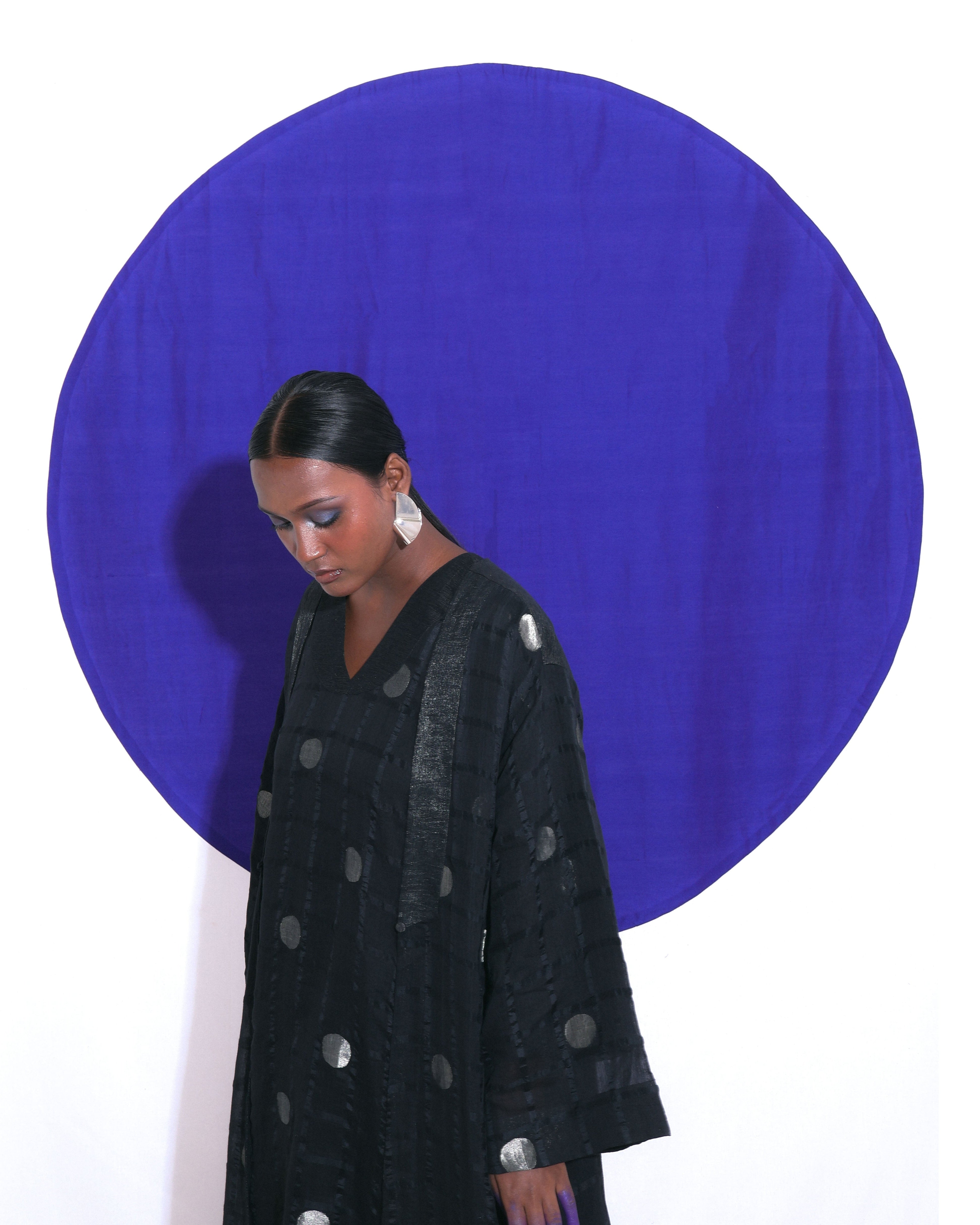 The Shoonyata Polka Dots Sheer Choga Overlay features an oversized, flowing silhouette made from handwoven silk. Crafted using intricate Jacquard Jamdani weaving techniques